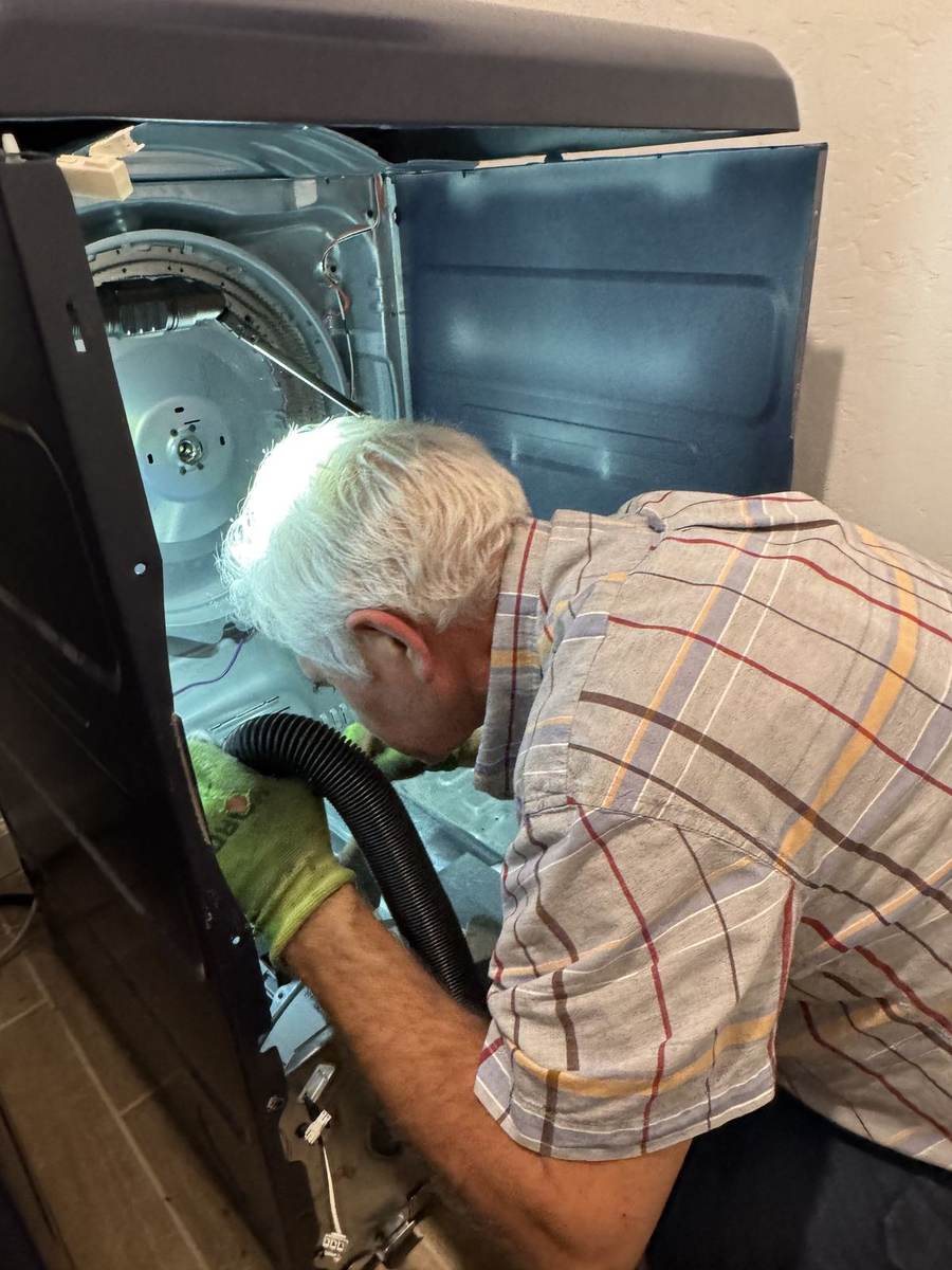 MVI technician vacuuming lint and debris from inside a dryer during maintenance
