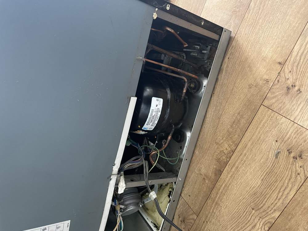Technician diagnosing a refrigerator compressor covered in dust